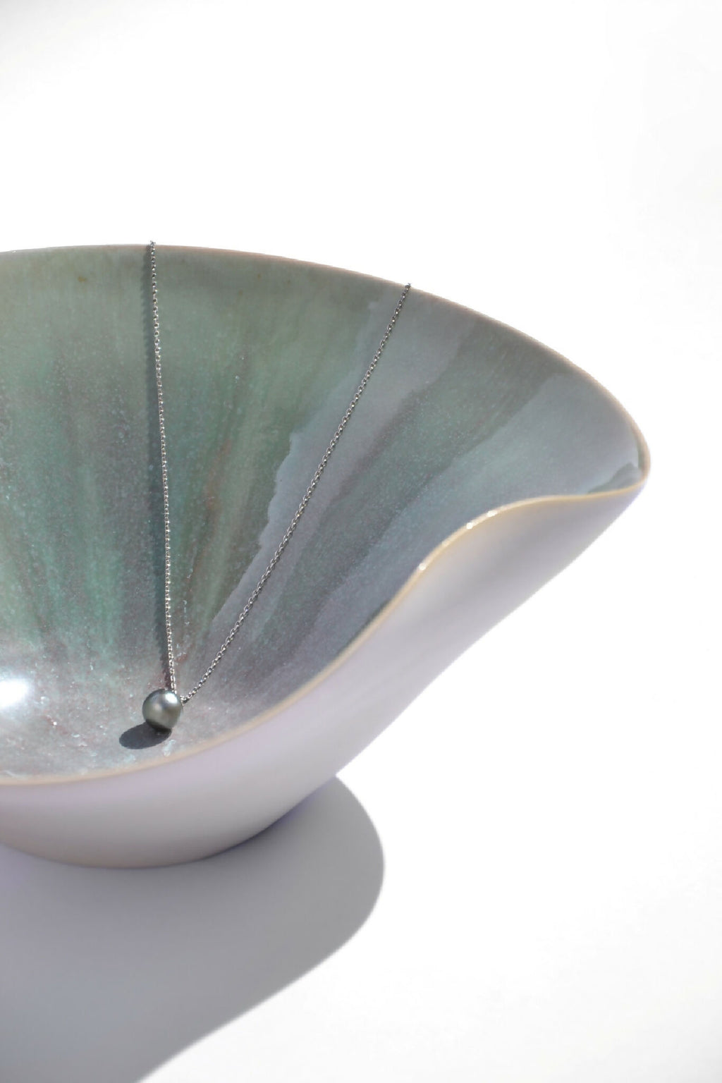 Coupe blanche avec intérieur vert marbré, collier fin et perle sombre sur le bord.