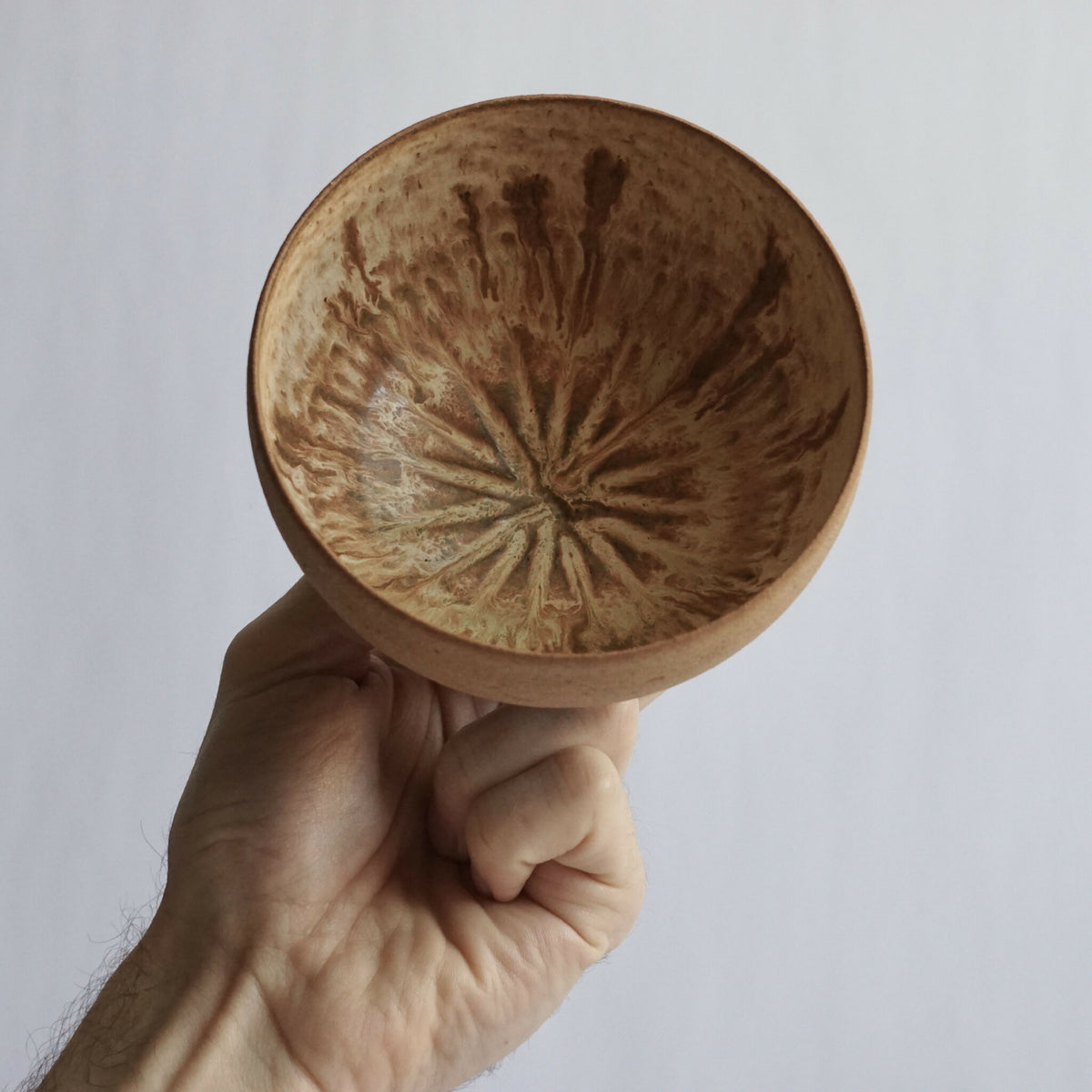 Bol en grès beige gravé, tenu dans la main, motif au fond visible.
