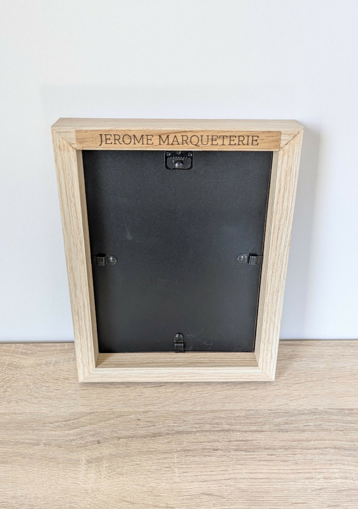 Dos de tableau marqueterie : cadre beige avec étiquette « JEROME MARQUETERIE » et attaches.