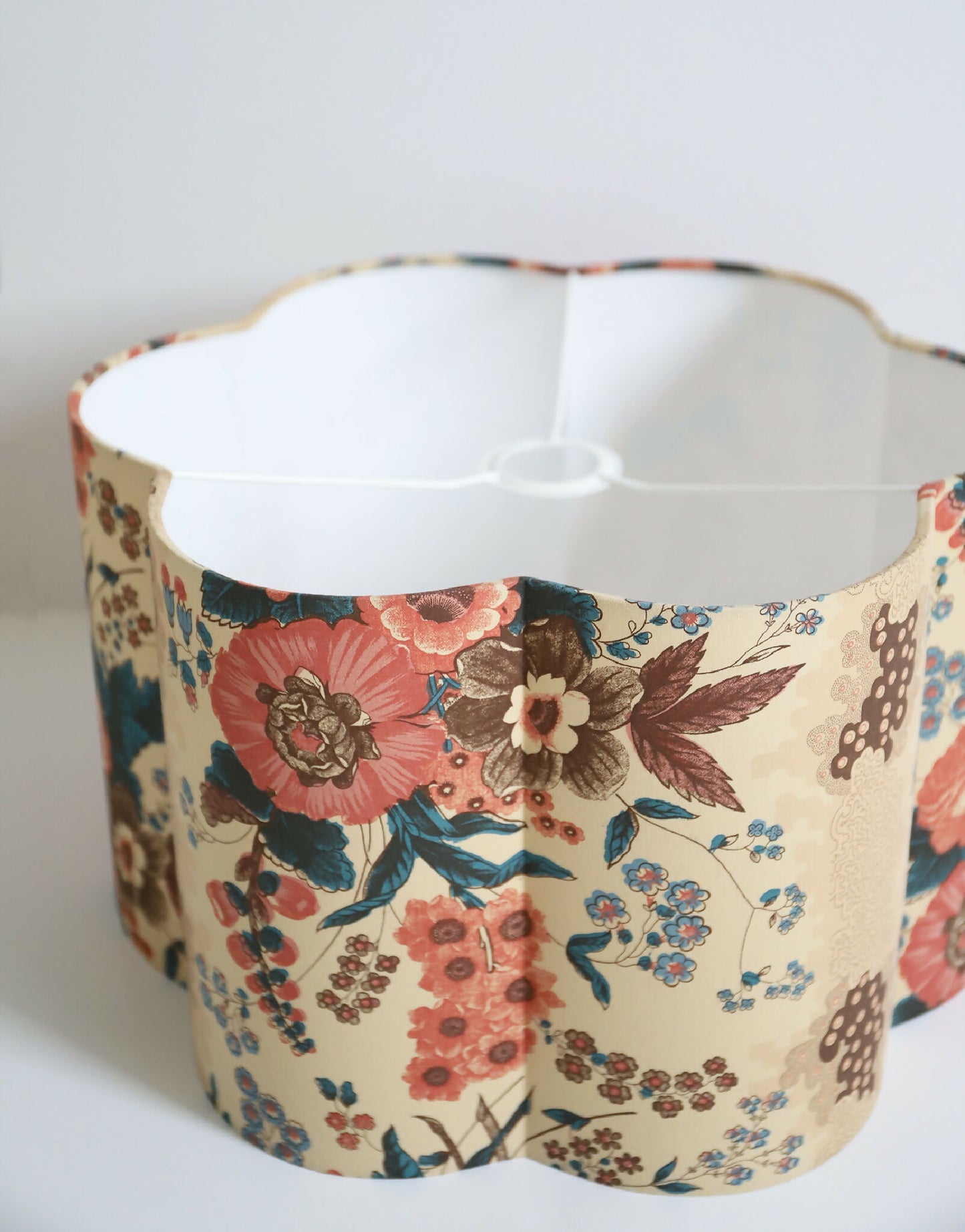 Abat-jour forme fleur, vue de dessus : intérieur blanc, bord ondulé, fleurs multicolores.