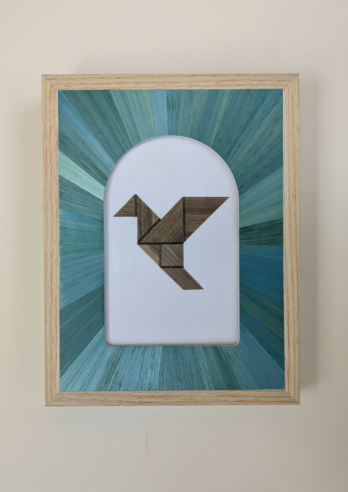 Tableau marqueterie en paille : oiseau géométrique brun et turquoise dans un cadre beige.