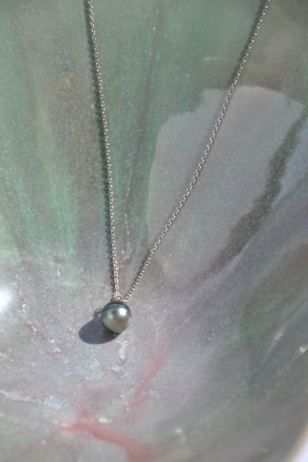 Coupe blanche à intérieur vert marbré, collier argenté et perle sombre au centre.
