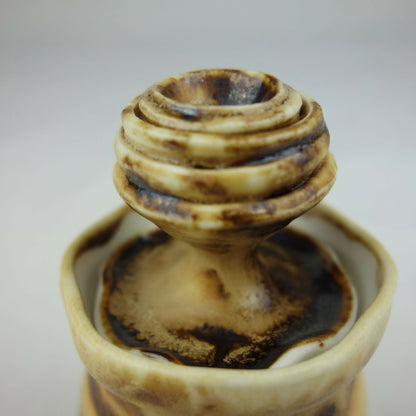 Haut d’un petit pot en céramique beige et brun, ouverture centrale et motifs foncés