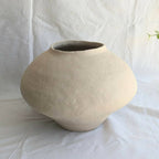 Vase en céramique beige, forme arrondie avec ouverture évasée.