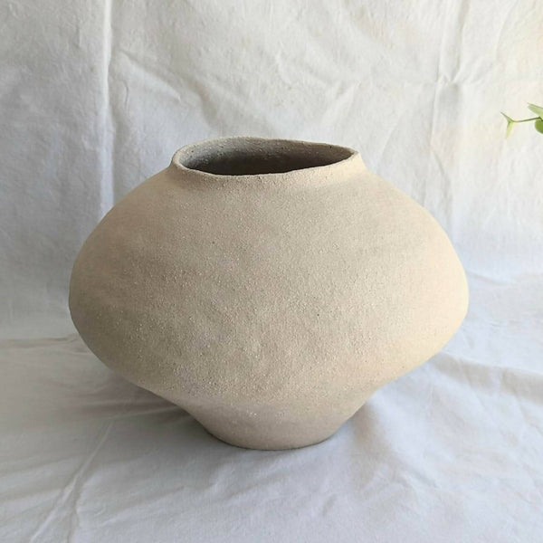 Vase en céramique beige, forme arrondie avec ouverture évasée.