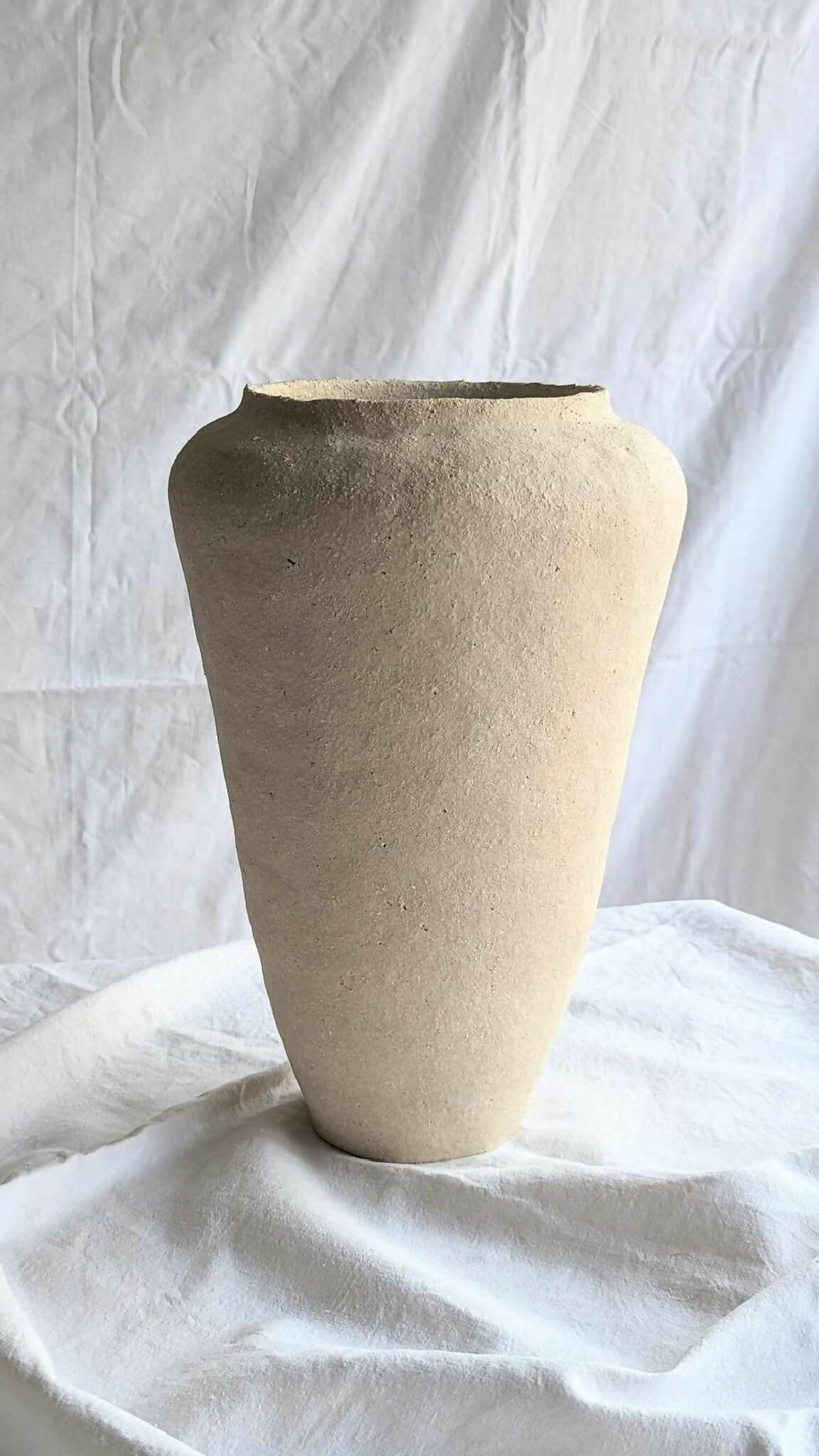 Vase en céramique beige à forme conique, ouverture large au bord sombre.