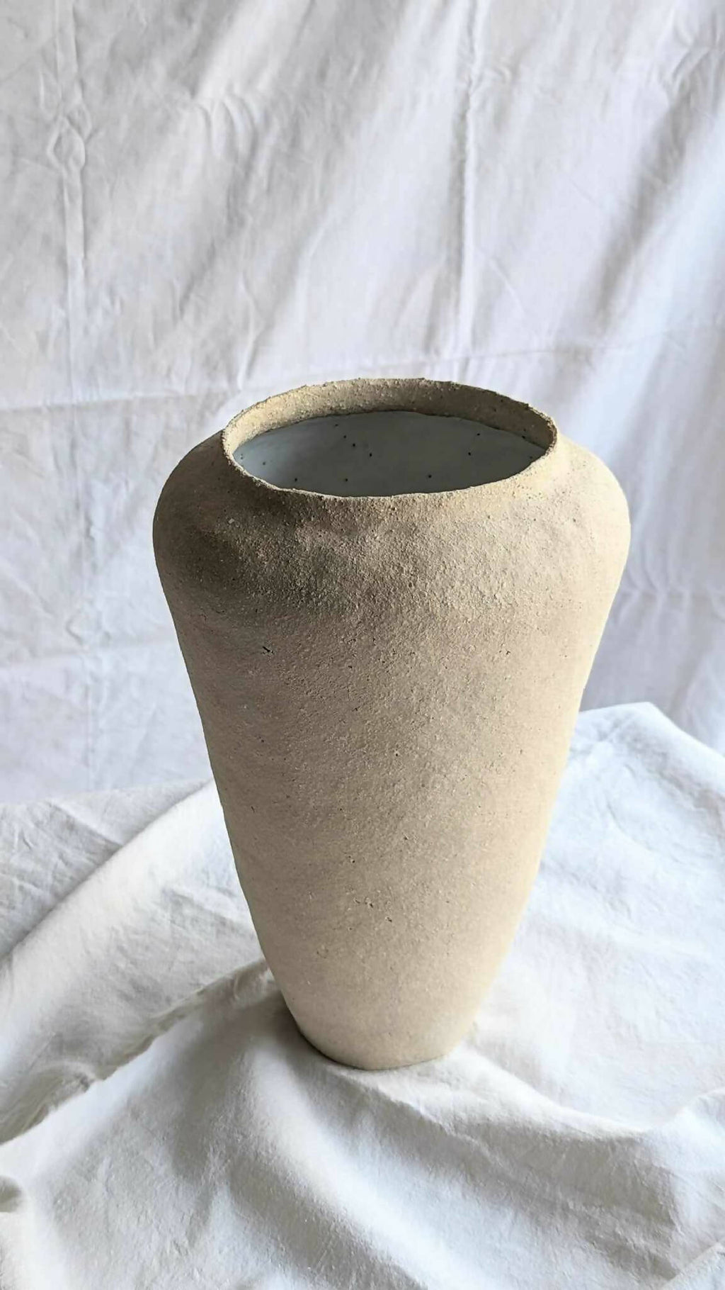 Vase beige en forme conique avec large ouverture circulaire, intérieur sombre.