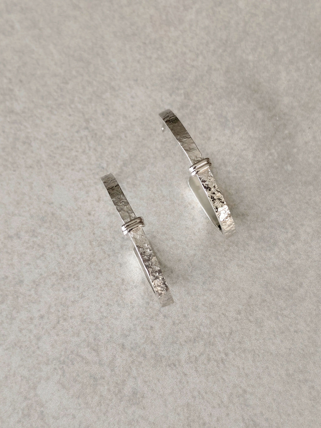 Boucles d’oreilles courbes argentées avec détails texturés, fermoirs visibles