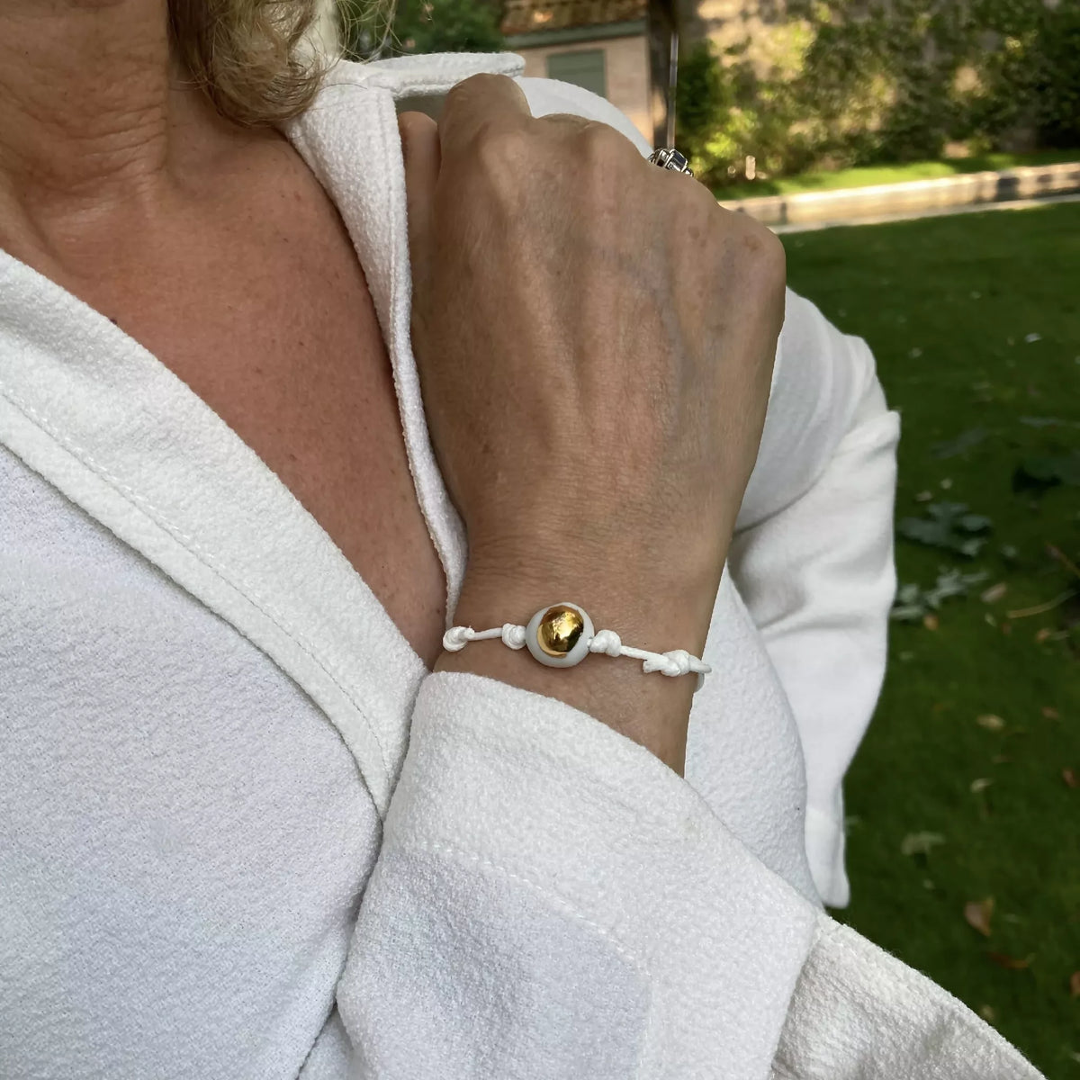 Bracelet au poignet : cordon blanc et perle dorée goutte sur tissu blanc