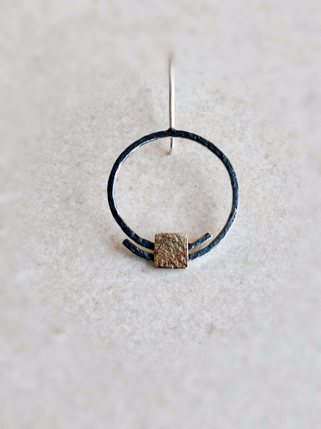 Boucles d’oreilles pendantes : anneau noir unique avec carré doré texturé et tige d’accroche.