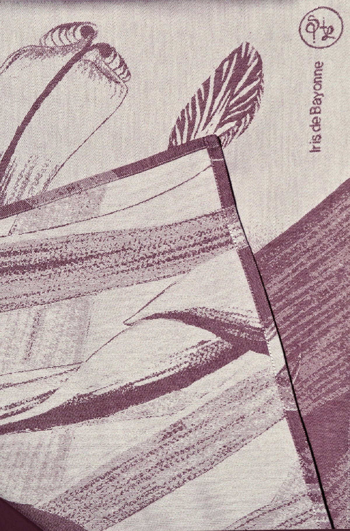 Détail de torchon imprimé : plumes et feuilles violet sur fond clair.