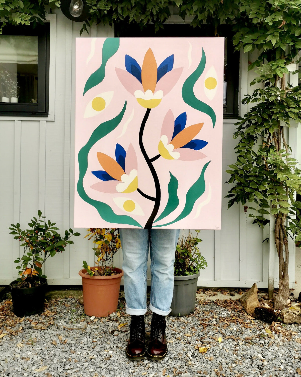 Peinture acrylique sur toile carrée posée dehors : fleurs stylisées orange, bleues et vertes