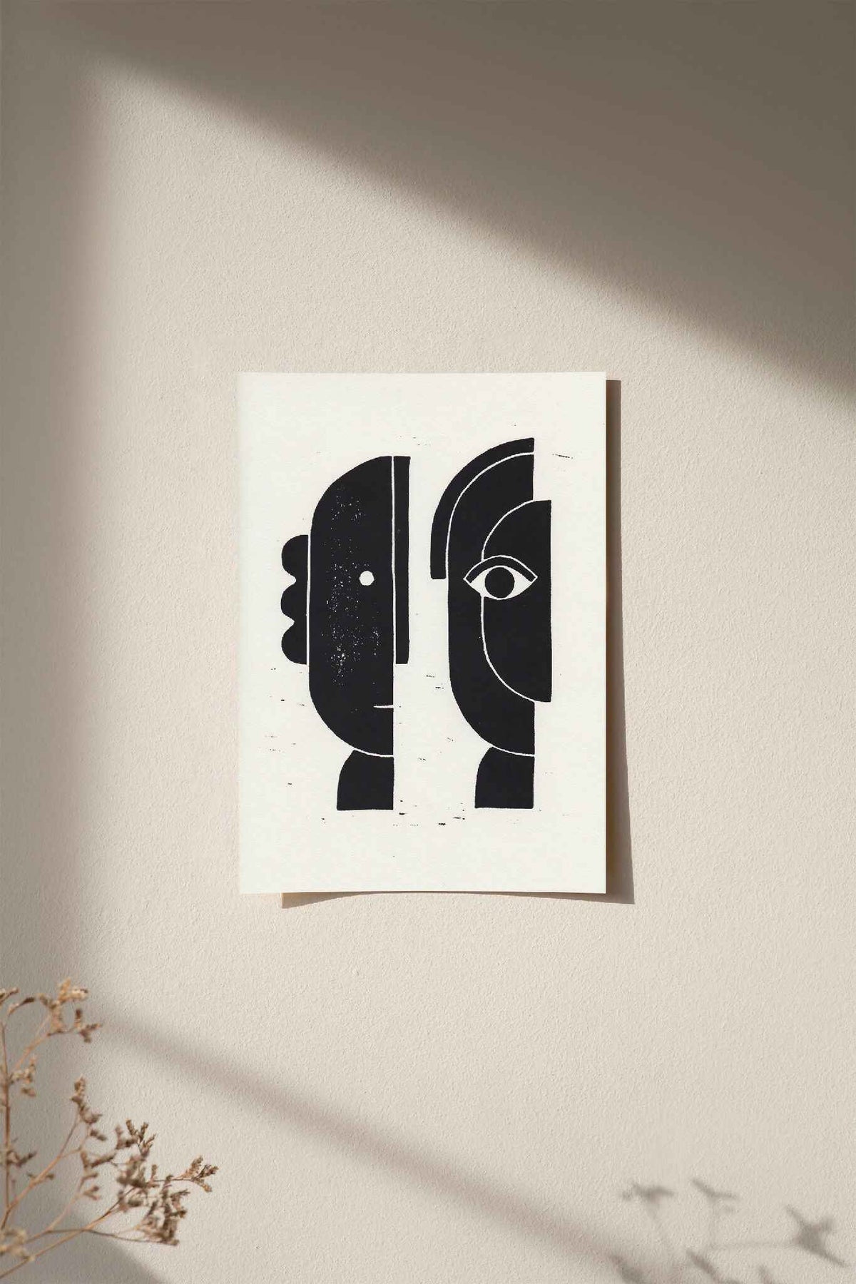 Linogravure encadrée, visages abstraits noirs sur fond clair.