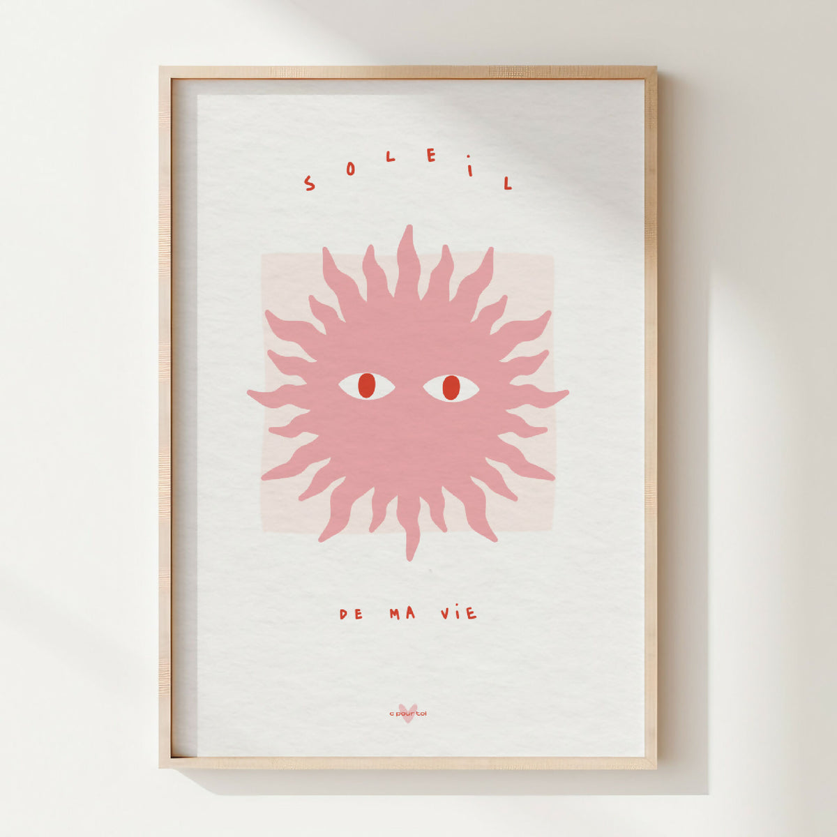 Affiche encadrée : soleil stylisé rose, yeux au centre, texte en haut et bas.