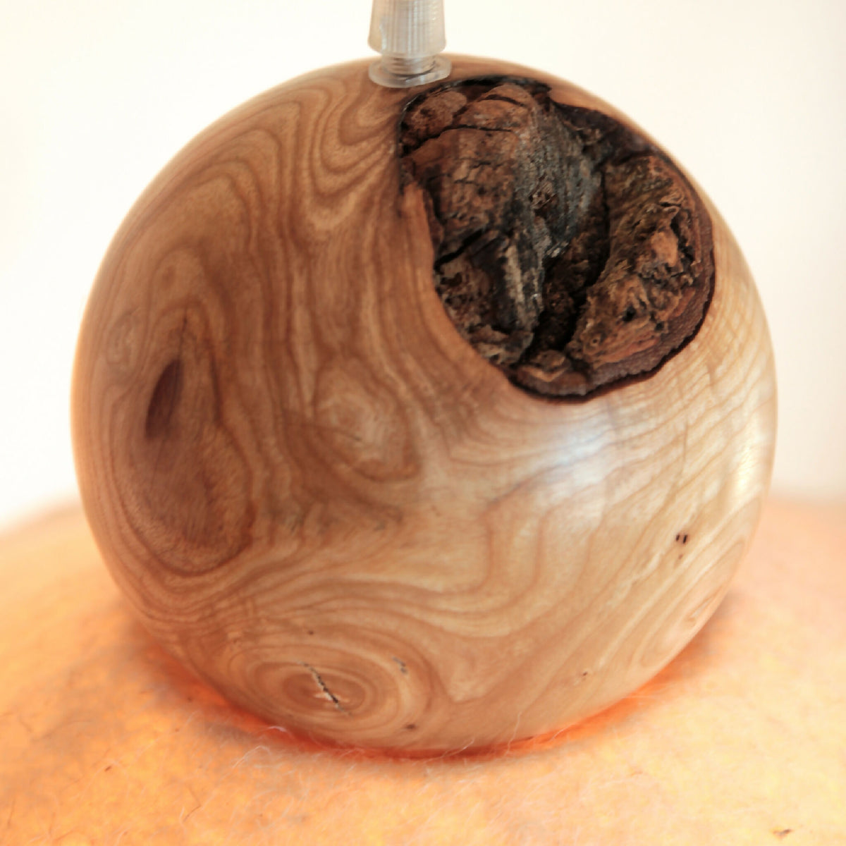 Sphère en bois veiné avec ouverture en feutre noir moucheté autour de l’ampoule.