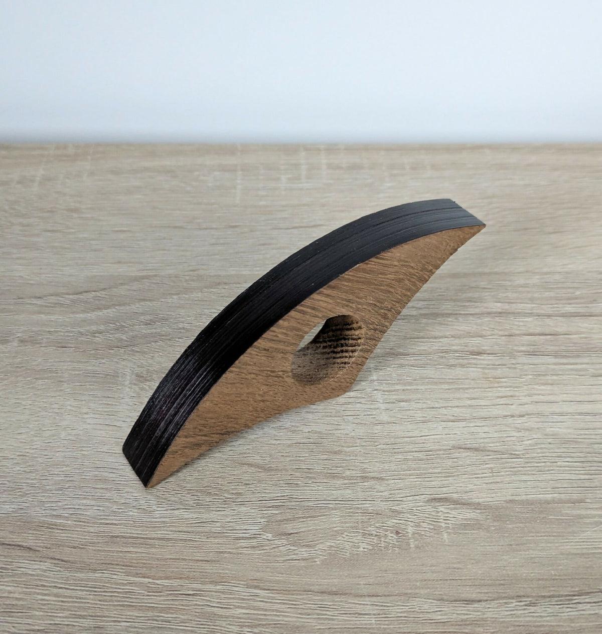 Accessoire de lecture en marqueterie, bande noire incurvée et insert brun, pose sur bois.