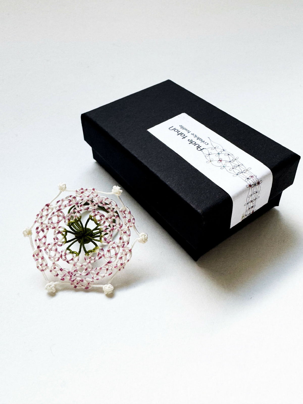 Bague en perles roses et blanches, motif trèfle vert, près d’une boîte cadeau noire