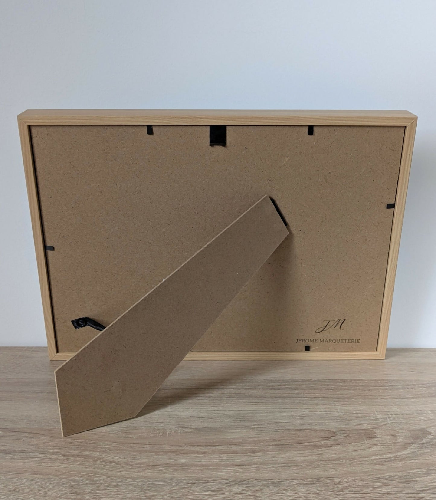 Dos du tableau encadré en bois clair avec accroche et étiquette de fabricant.