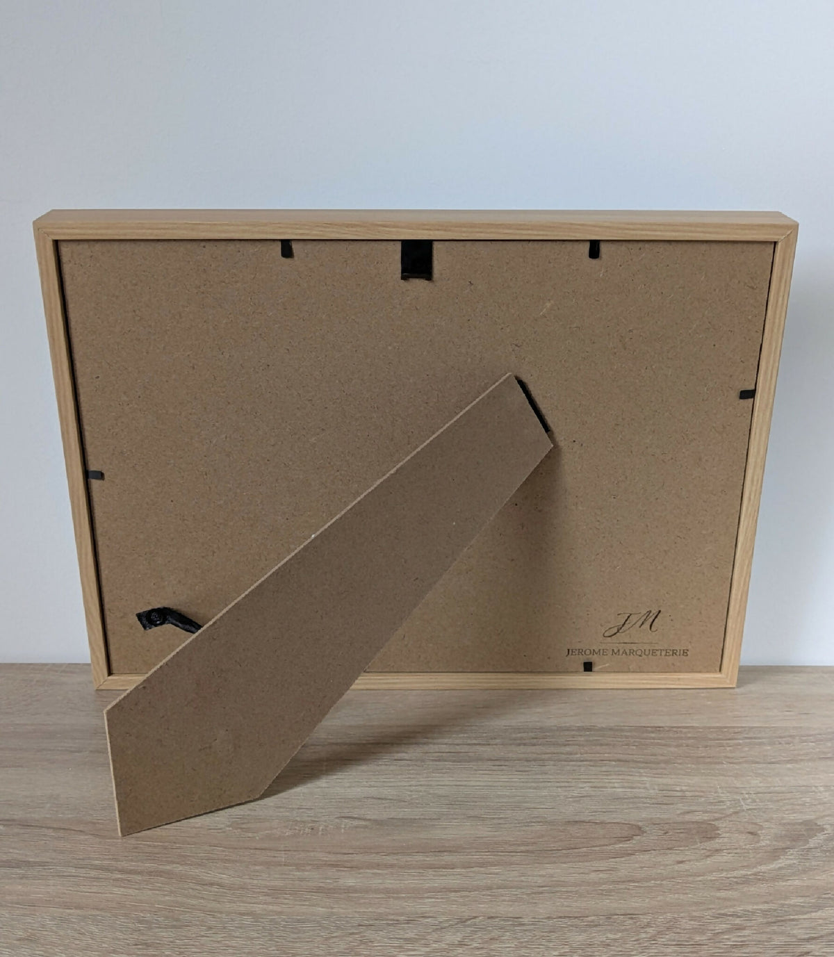 Dos du tableau encadré en bois clair avec accroche et étiquette de fabricant.