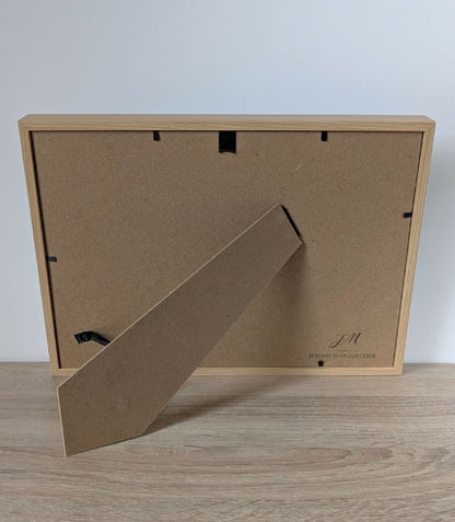 Dos du tableau encadré en bois clair avec accroche et étiquette de fabricant.