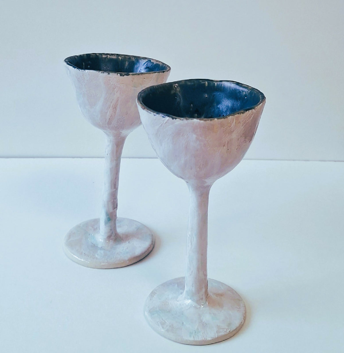 Deux verres à pied texturés, bords bleu foncé et coupes blanches sur tiges