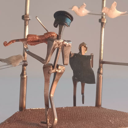 Figurines en métal doré sur manège décoratif, musicien et silhouette en robe noire.
