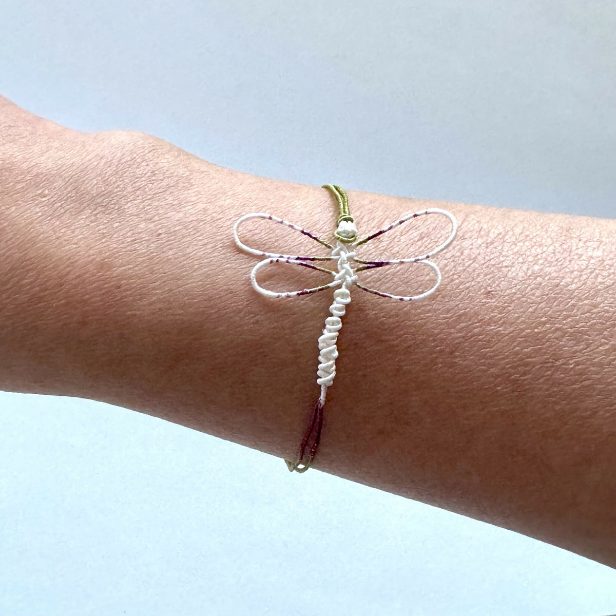 Bracelet libellule sur poignet, cordon blanc avec ailes striées rouge et vert