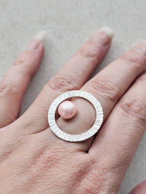 Bague Atoll argentée avec cabochon perle rose et anneau strié, portée sur la main