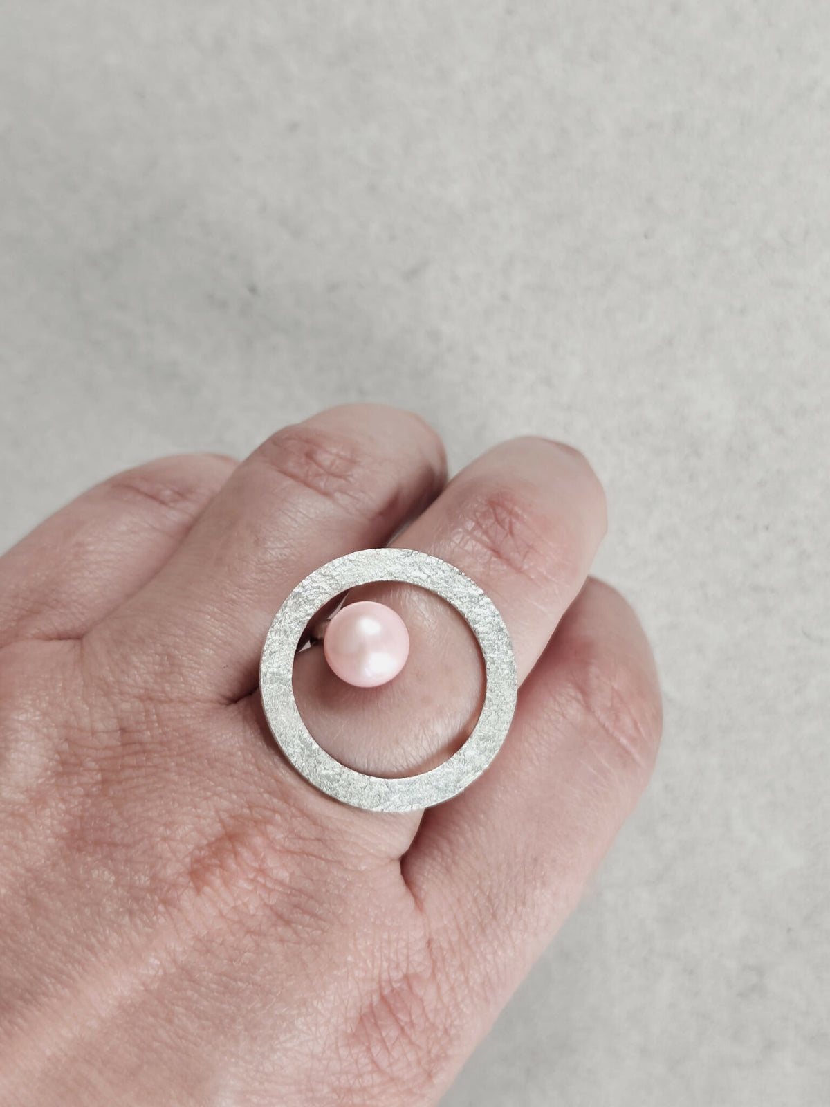 Bague Atoll sur main, anneau argenté texturé et cabochon perle rose