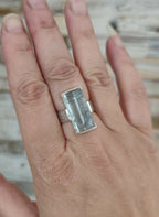 Bague en topaze bleu clair rectangulaire sur la main, monture argent.
