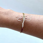 Bracelet libellule sur poignet, cordon blanc avec ailes striées rouge et vert
