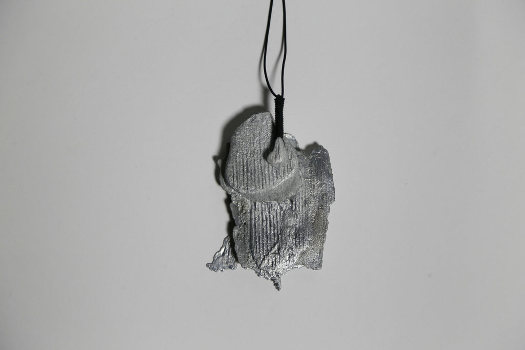 Pendentif gris en forme de feuille d’arbre, vue de trois-quarts, sur cordon.