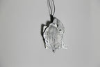 Pendentif argenté-gris en forme de feuille, vue rapprochée et inclinée, cordon noir.