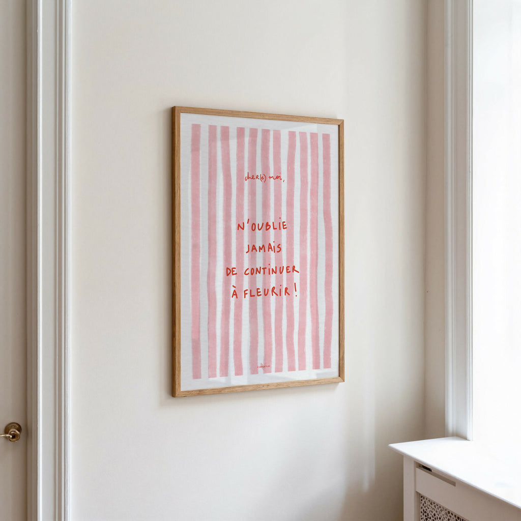 Affiche encadrée sur mur, rayures verticales roses et citation manuscrite « À fleurir »