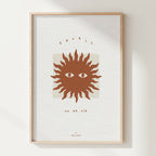 Affiche encadrée : soleil stylisé brun, deux yeux, typographie en haut et bas.