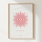 Affiche encadrée : soleil stylisé rose, yeux au centre, texte en haut et bas.