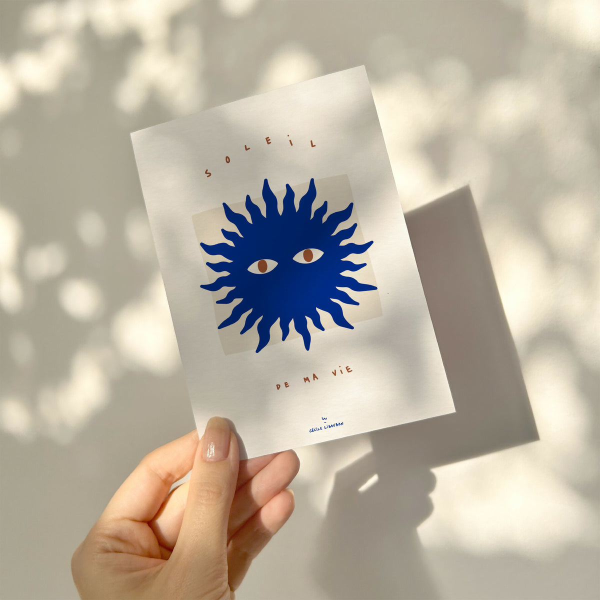 Carte à message blanche avec soleil bleu, visages et « de ma vie », tenue en main