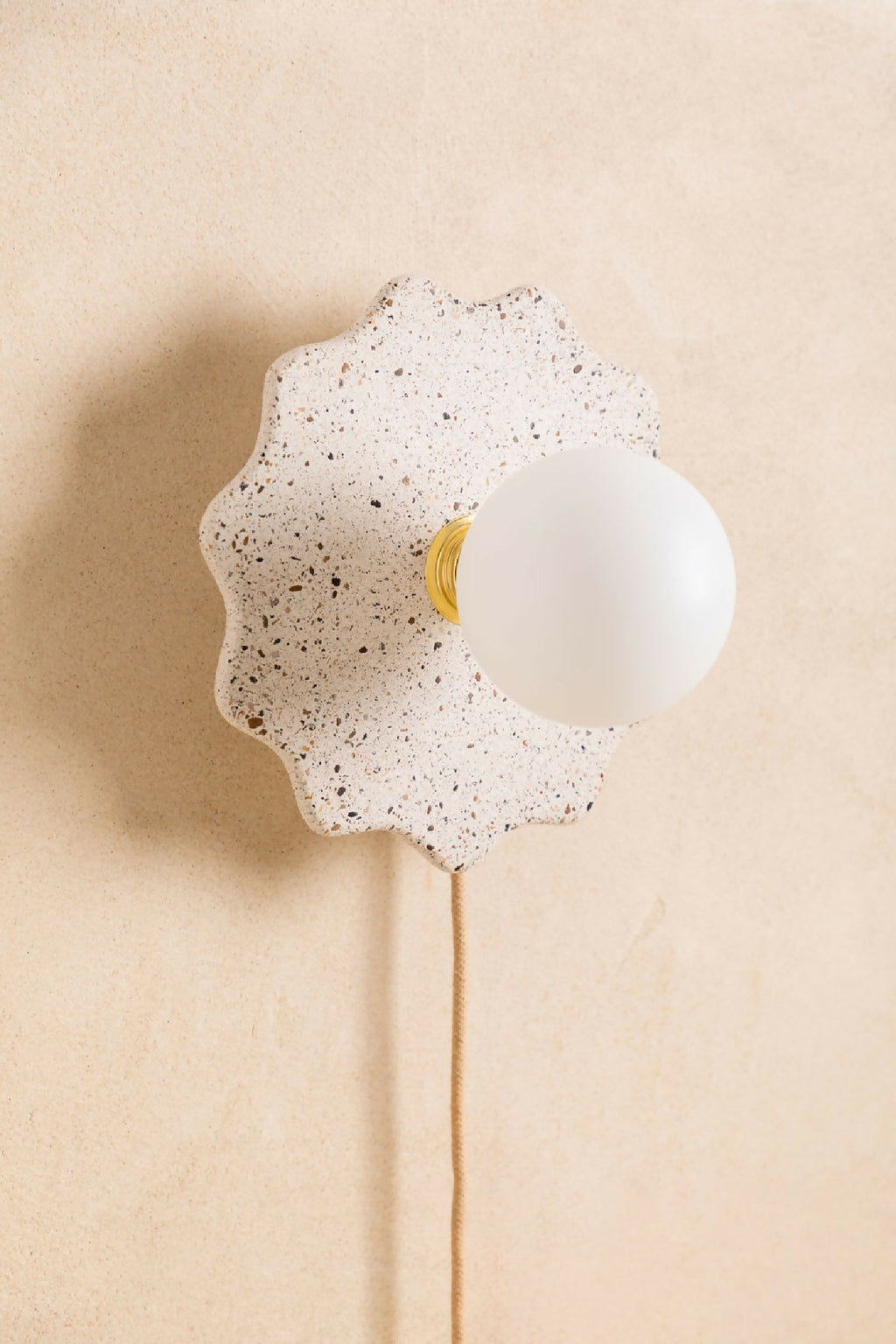 Applique murale en forme de fleur crème tachetée, globe blanc avec liseré jaune.