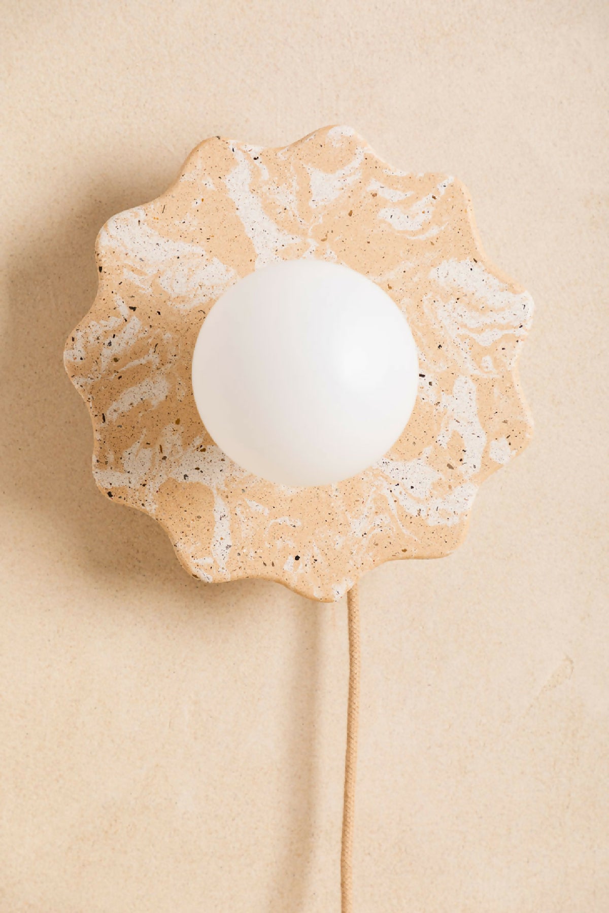 Applique murale en forme de fleur beige clair tachetée, globe blanc et câble.