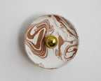 Applique murale ronde marbrée beige et blanc, avec un bouton doré au centre.