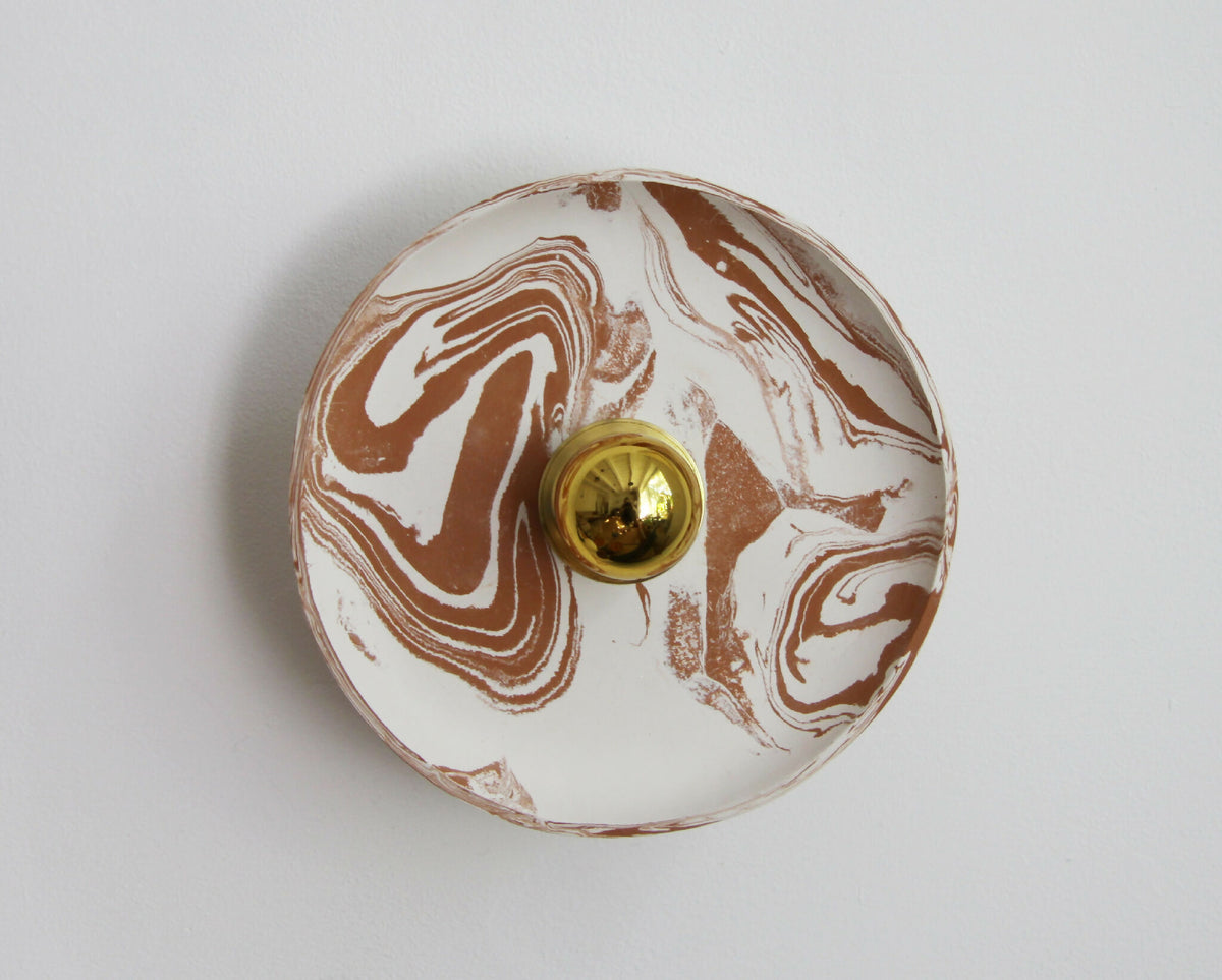 Applique murale ronde marbrée beige et blanc, avec un bouton doré au centre.