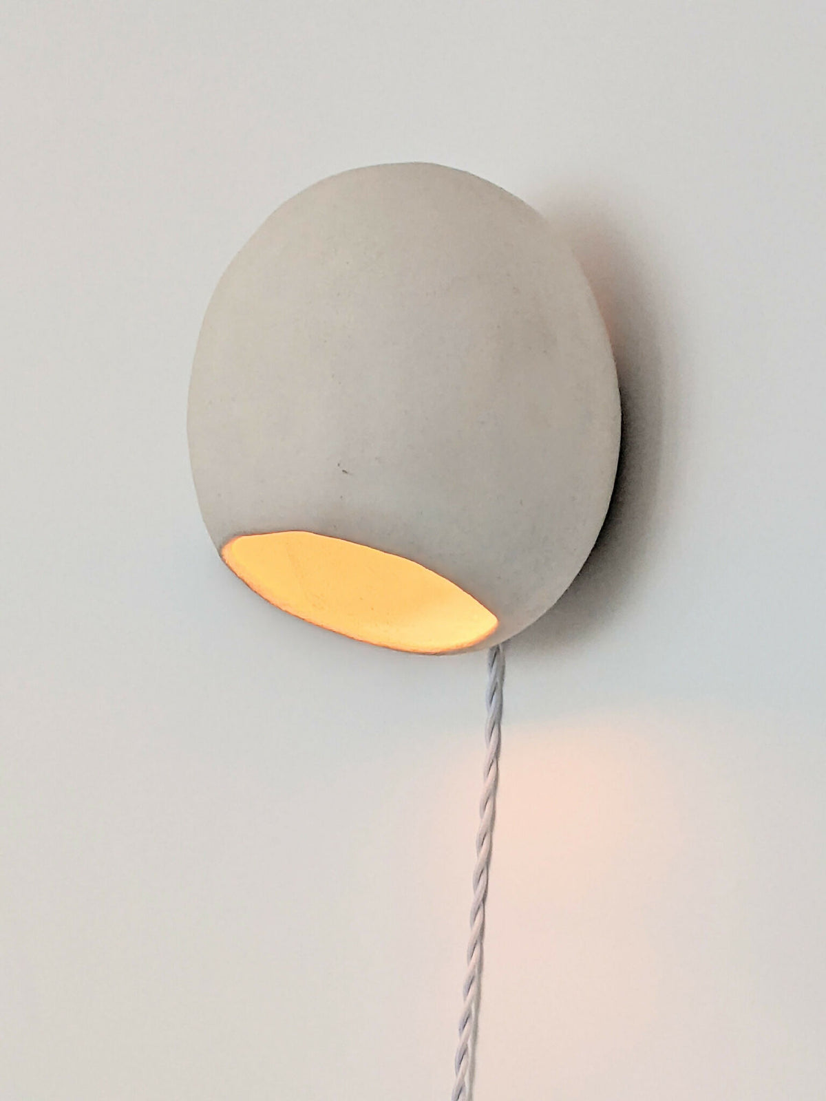 Applique en céramique ronde grise, lumière orange, sur un câble torsadé blanc