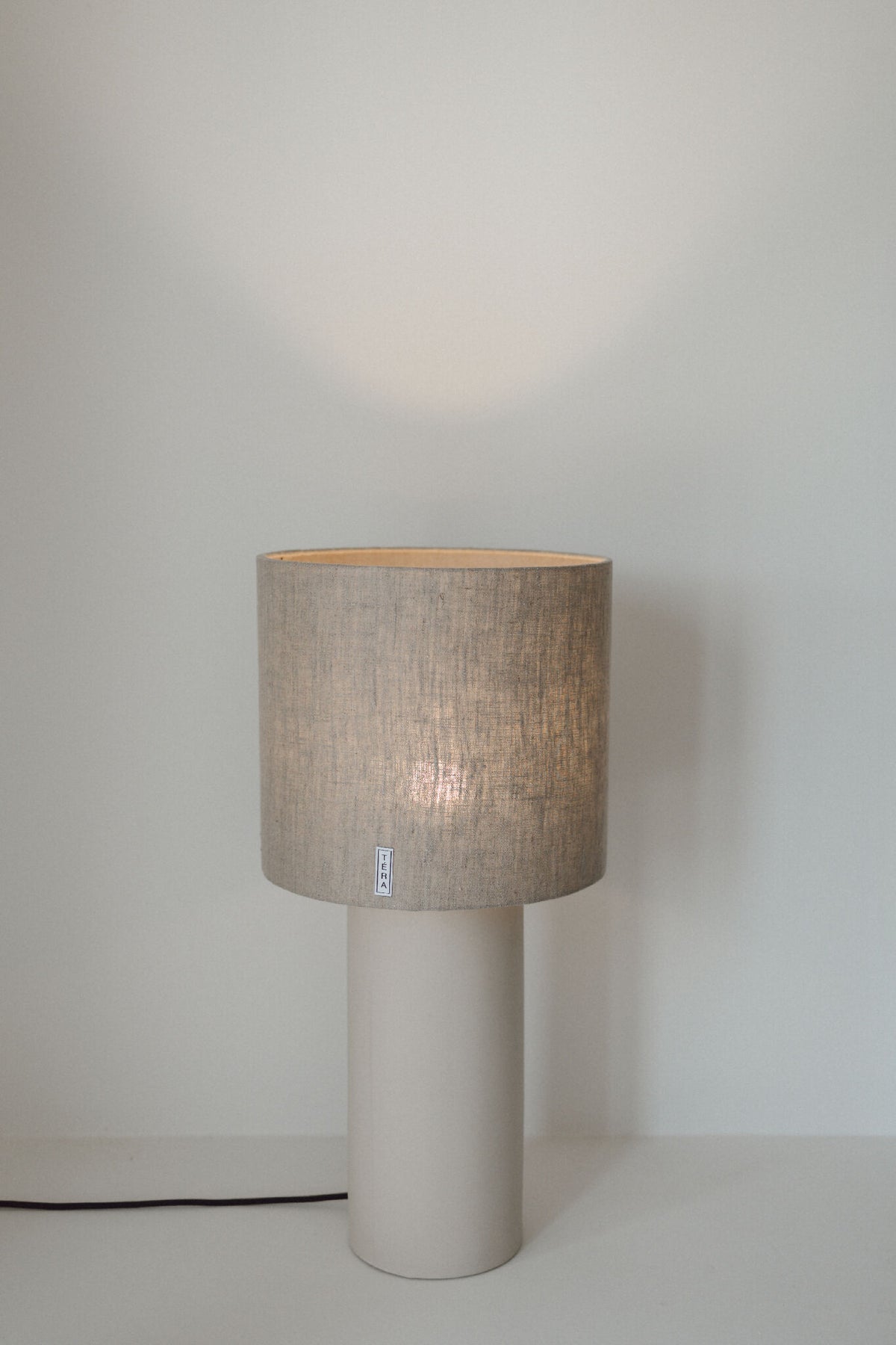 Lampe TERA avec base blanche cylindrique et abat-jour en tissu beige, vue de face