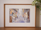 Impression d’art encadrée : ruelle pastel avec panneaux et lanternes orange.