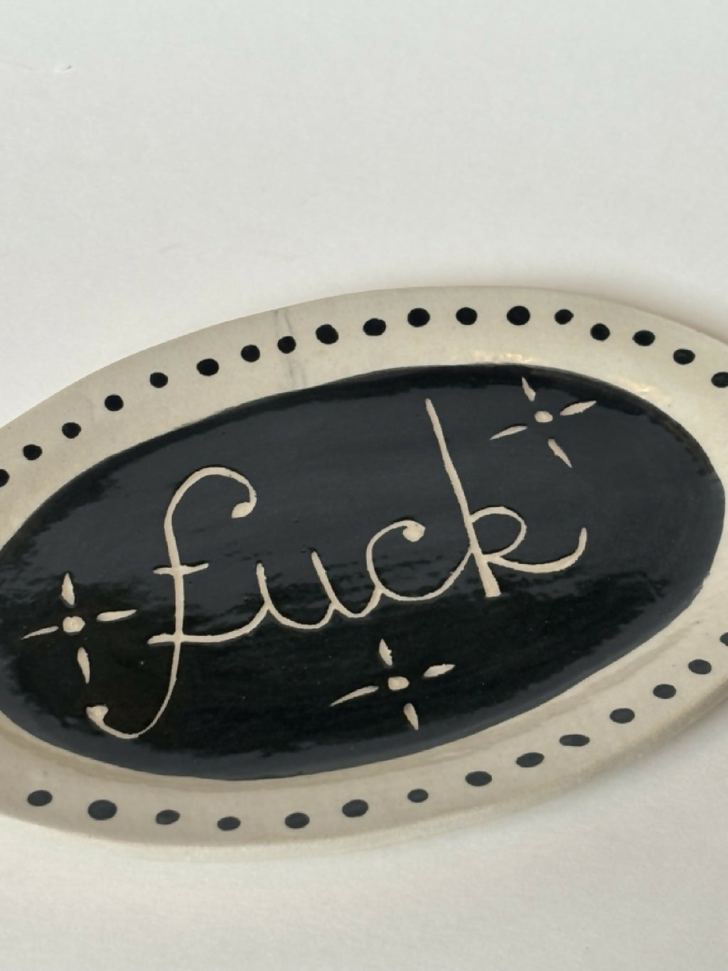 Assiette ovale noire avec texte 'fuck' doré, liseré de pois et détails étoiles.