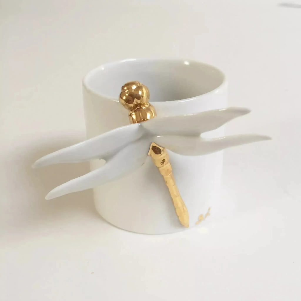 Tasse blanche avec tête de libellule dorée et ailes sculptées, vue de trois-quarts