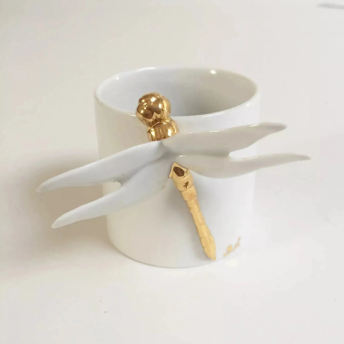 Tasse blanche avec tête de libellule dorée et ailes sculptées, vue de trois-quarts