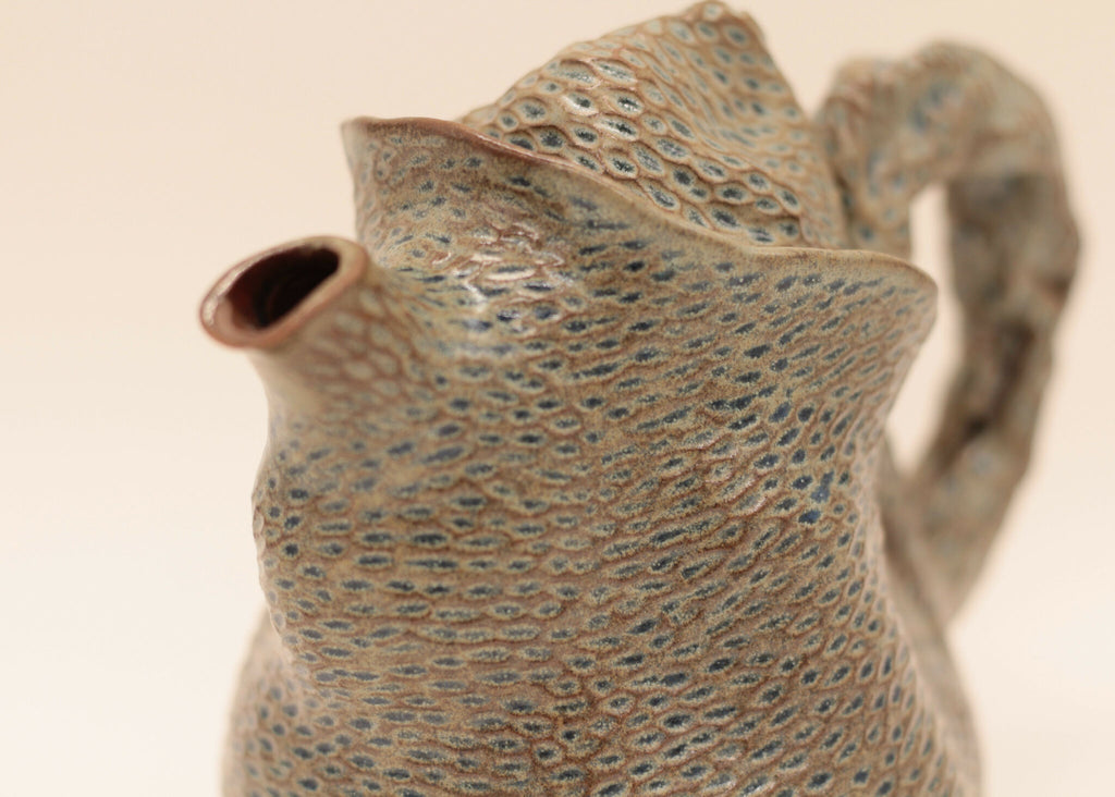 Théière en céramique bleu-gris, gros plan du bec et du motif en relief