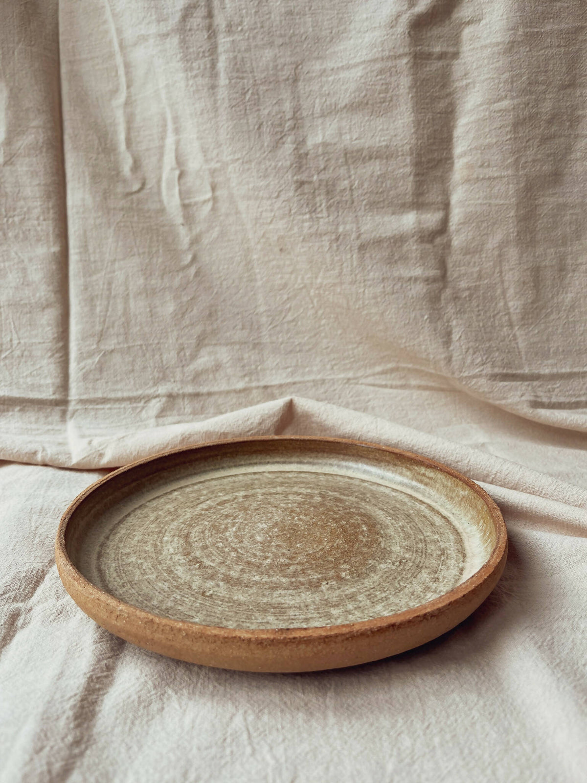 Assiette creuse en céramique beige à bord brun, vue de dessus, finition texturée