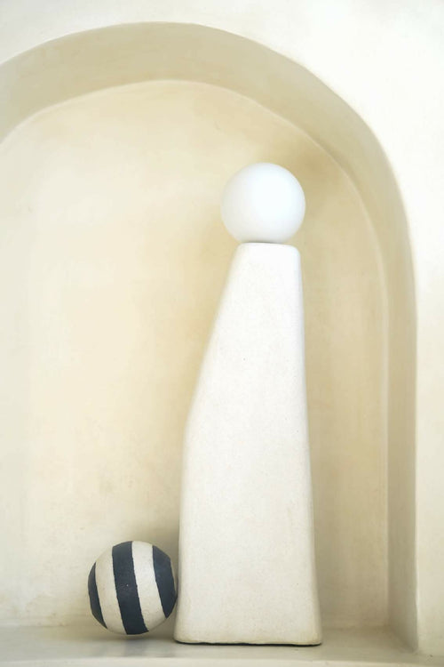Sculpture lumineuse blanche dans une niche, sphère supérieure et boules rayées noir et blanc.